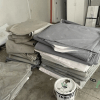 Stacks of folded grey fabric next to a paint bucket in a storage area.