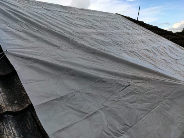 Grey tarp secured over a tiled roof