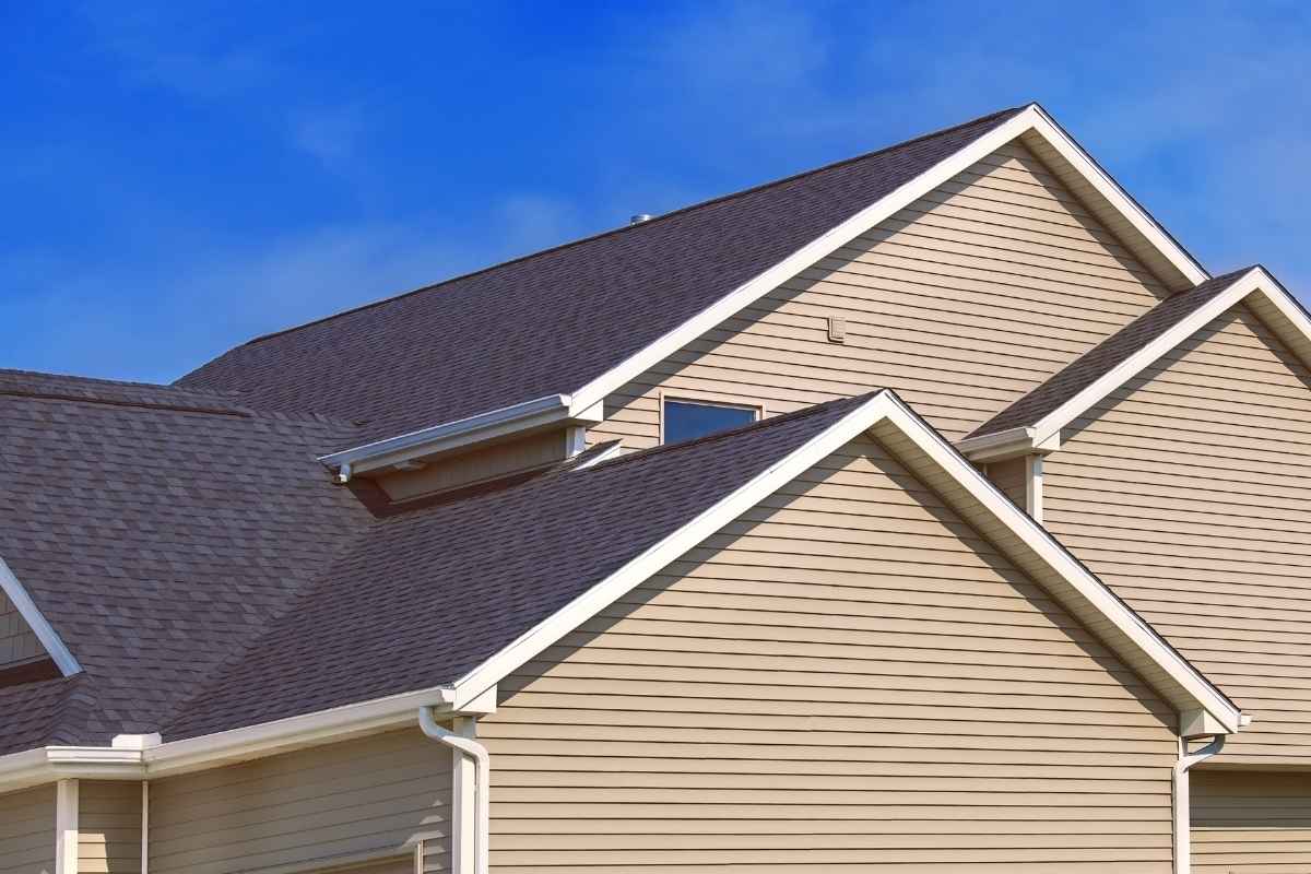 A beige house with multiple pitched roofs and dark shingles