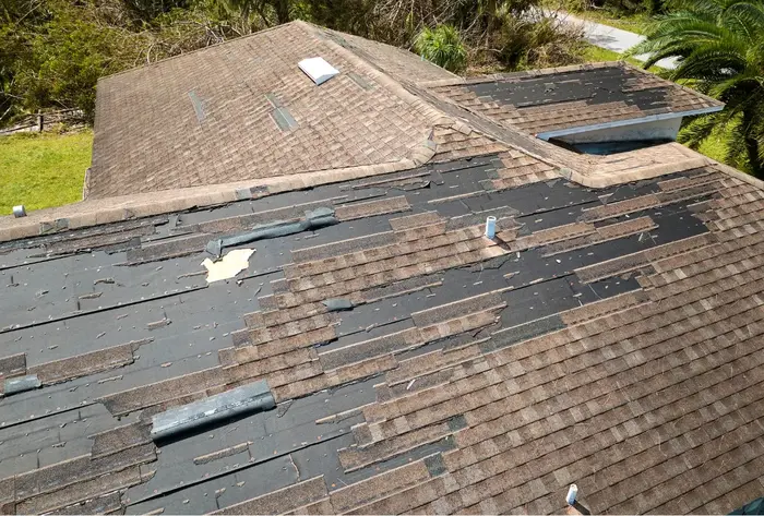 Roof with missing and damaged shingles showing exposed underlayment