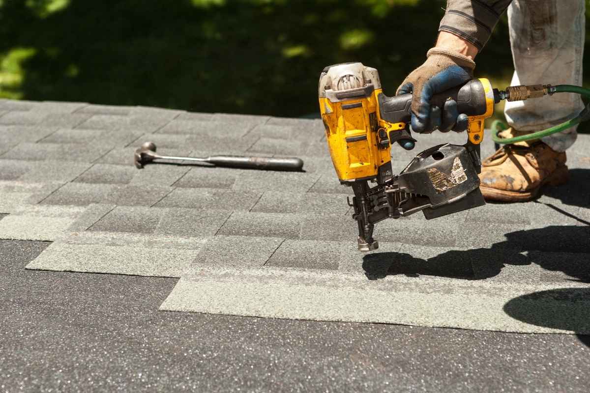 Worker using a nail gun to install shingles on a roof.