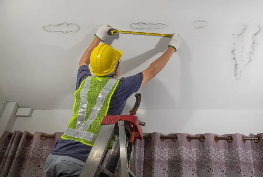 Worker measuring ceiling damage from roof leaks.